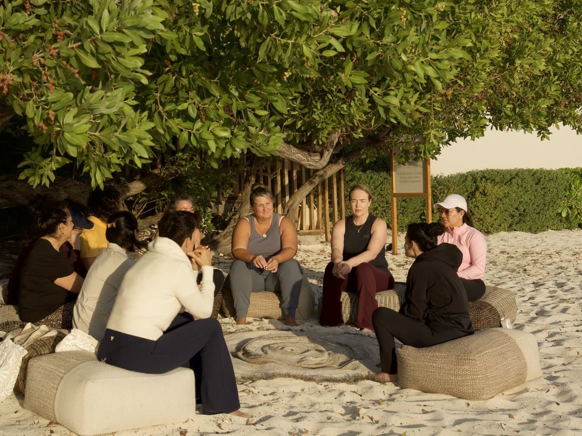 Guests sitting in a circle on the sand, under a tree by the beach