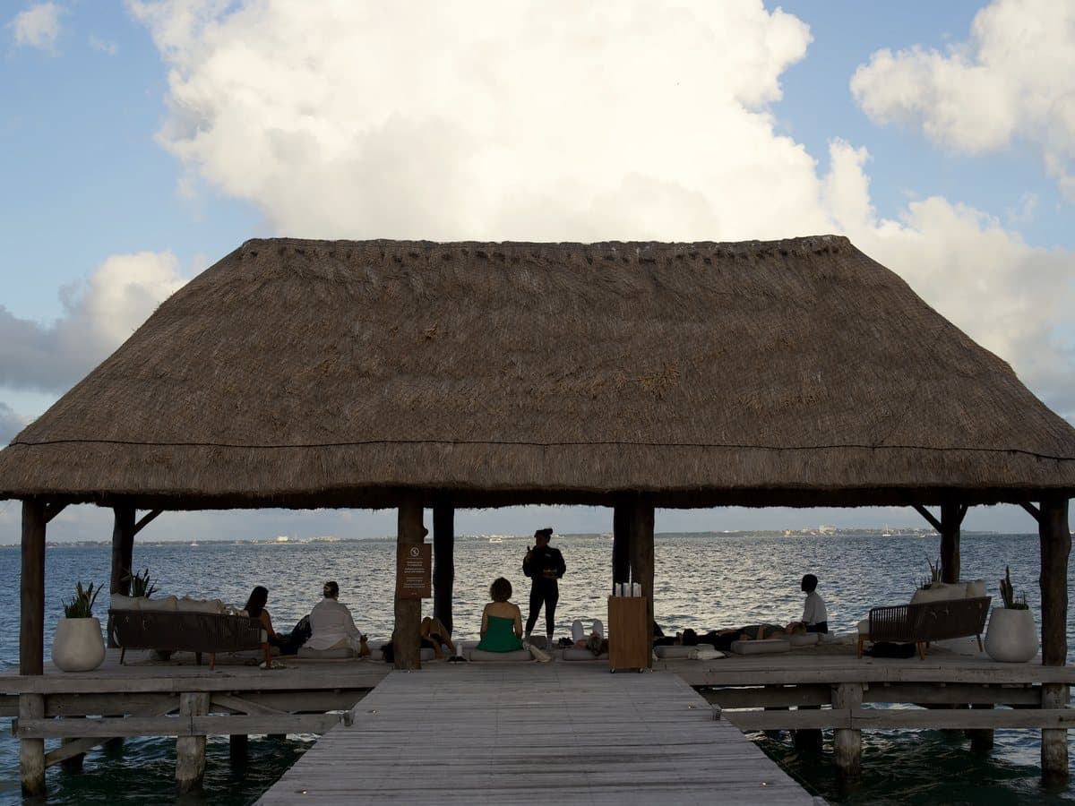 Guests on mats under a thatched palapa at the end of a pier over the sea
